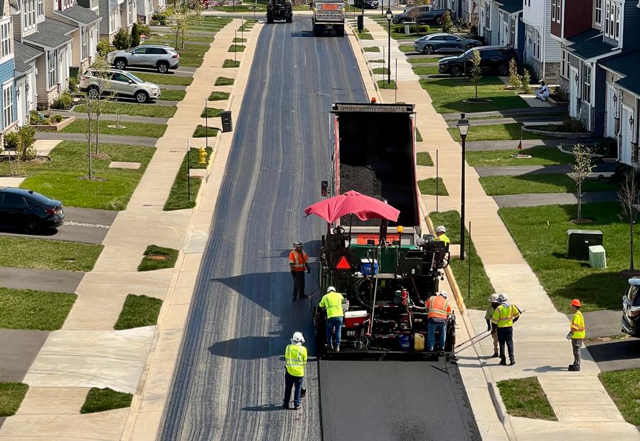 Paver laying a fresh mat of hot mix down a residential street with the crew walking alongside