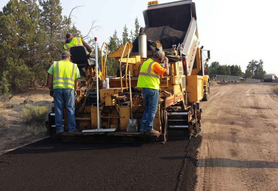 Crew riding the paver as it lays the first course of asphalt over a compacted gravel base