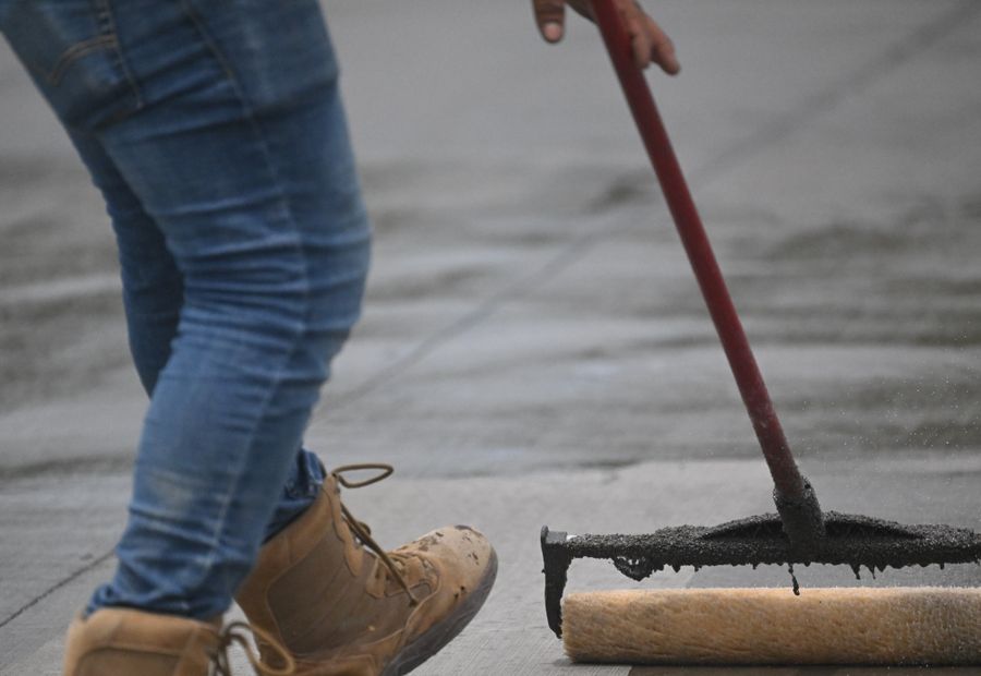 Worker pulling a squeegee of black sealer across a driveway surface